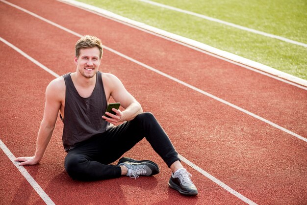 Retrato de un hombre sonriente sentado en la pista roja con teléfono móvil en la mano