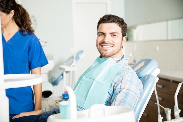 Retrato de un hombre sonriente sentado en una silla mientras una dentista trabaja en la clínica