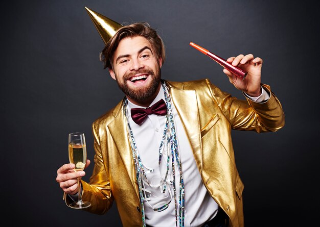 Retrato de hombre sonriente sosteniendo flauta de champán y soplador de fiesta