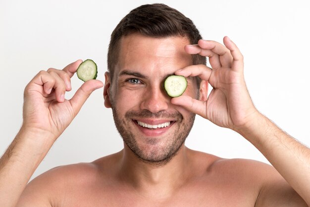 Retrato de hombre sonriente sosteniendo y ocultando los ojos con una rodaja de pepino