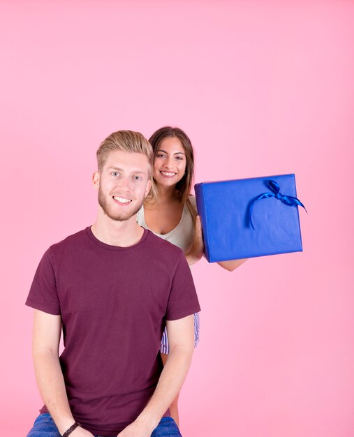 Retrato de hombre sonriente con su novia detrás de la celebración de caja de regalo azul