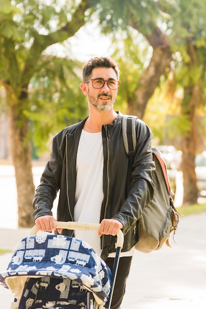 Foto gratuita retrato de un hombre con su mochila caminando con un cochecito de bebé en el parque