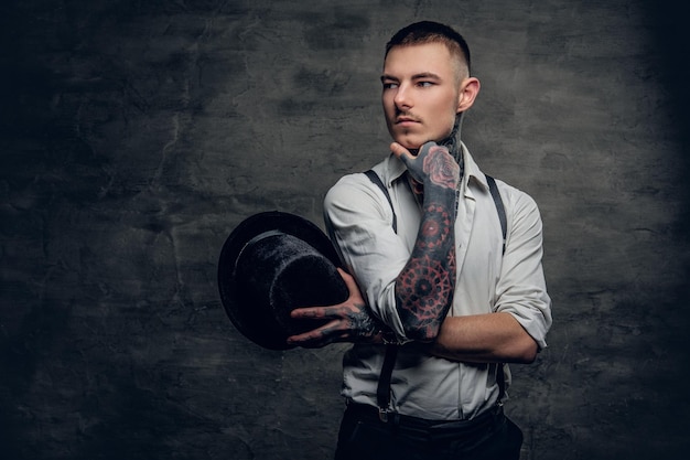 Retrato de un hombre tatuado con camisa blanca y tirantes.