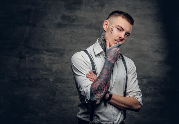Retrato de un hombre tatuado con camisa blanca y tirantes.