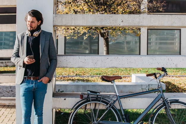 Retrato de un hombre con teléfono celular en la mano de pie cerca de la bicicleta