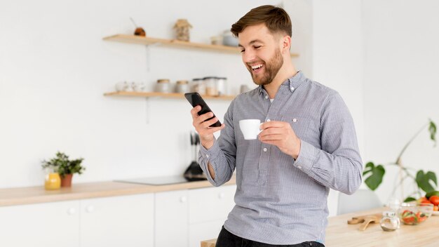 Retrato hombre tomando café mientras revisa móvil