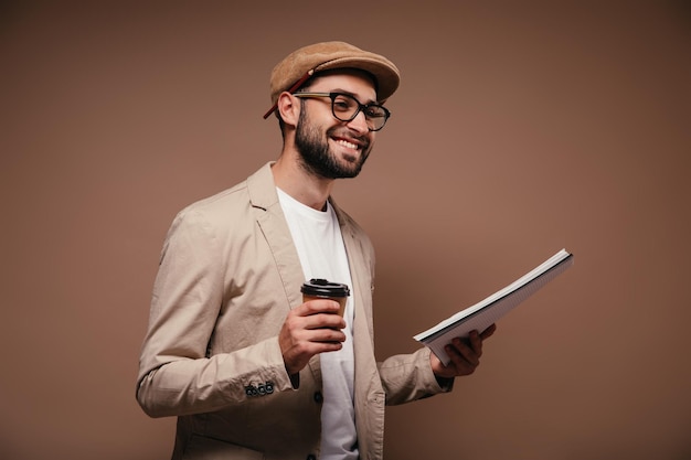 Retrato de hombre con traje beige sosteniendo un vaso de té y un cuaderno