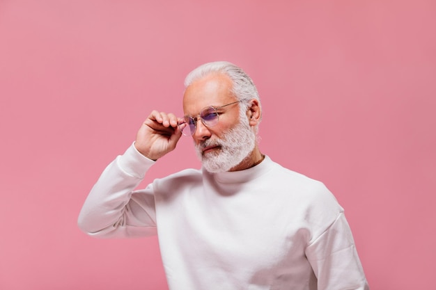 Retrato de hombre en traje blanco sobre fondo rosa Chico guapo de pelo gris con barba en anteojos posando sobre fondo aislado