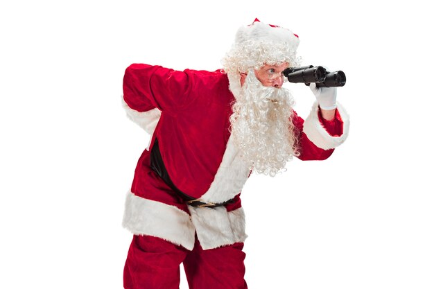 Retrato de hombre en traje de Papá Noel con una lujosa barba blanca, sombrero de Papá Noel y un traje rojo - en longitud completa aislado en blanco con binoculares