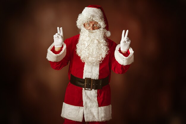 Foto gratuita retrato de hombre en traje de santa claus - con una lujosa barba blanca, sombrero de santa y un traje rojo en el fondo rojo del estudio