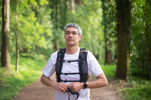 Retrato de un hombre tranquilo caminando por el bosque. Hombre adulto medio con gafas con mochila pasando tiempo al aire libre. Naturaleza, trekking, concepto de ocio.