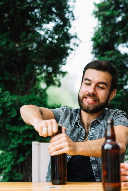 Retrato de un hombre tratando de abrir la tapa de la botella de cerveza