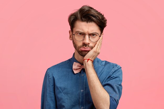 Retrato de hombre triste y estresante mantiene la mano en la mejilla, mira desesperadamente, siente dolor de muelas, tiene algunos problemas