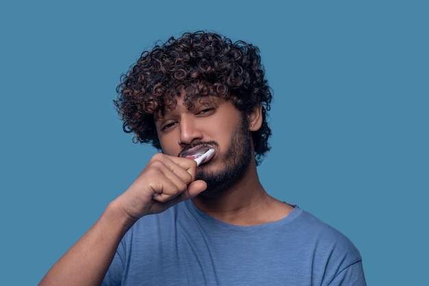 Retrato de un hombre triste y soñoliento cepillándose los dientes con pasta de dientes blanca y un cepillo de dientes de plástico