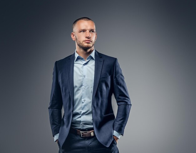 Retrato de un hombre vestido con un elegante traje azul sobre fondo gris.