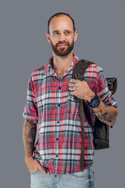 Retrato de un hombre viajero barbudo con mochila aislado sobre fondo gris.