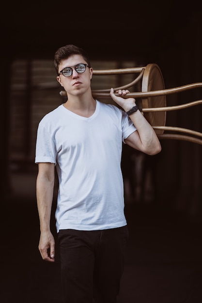 Retrato de hombres de pie con silla en camiseta blanca y gafas de sol en la calle