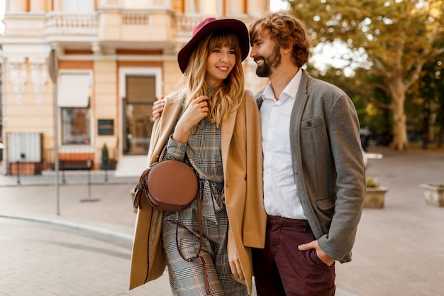 Retrato de una increíble pareja elegante enamorada de pasar unas vacaciones románticas en la ciudad europea de cerca. Mujer bonita rubia con sombrero y vestido casual sonriendo y mirando a su guapo hombre con barba.
