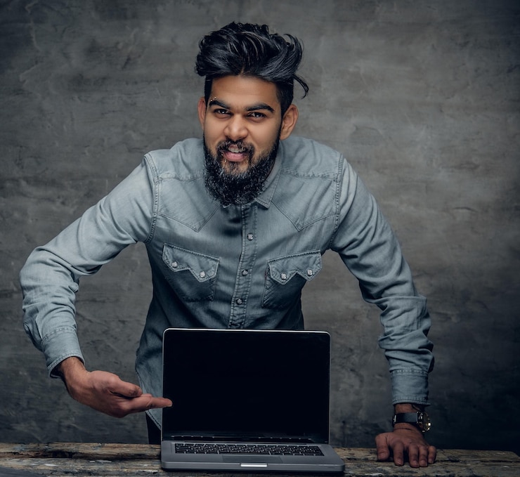 Foto gratuito retrato de un indio barbudo cerca de la mesa con una laptop encima.