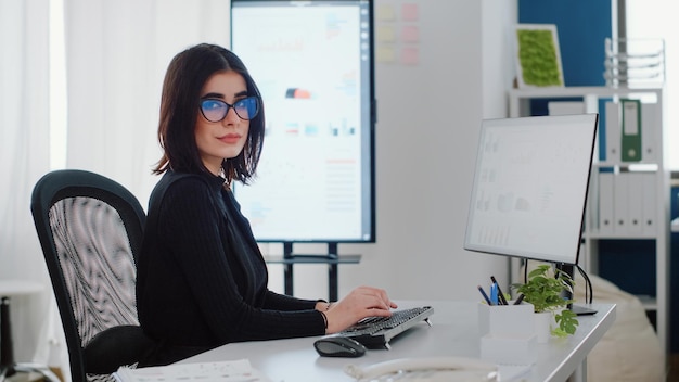 Foto gratuita retrato de ingeniero con computadora para el diseño de gráficos en el escritorio. empresaria mirando a cámara y trabajando con monitor para planificación de proyectos. persona con trabajo corporativo en la oficina de la empresa.