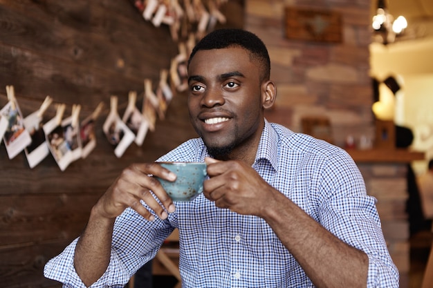 Retrato interior de apuesto joven empresario de piel oscura u oficinista sosteniendo una taza de café