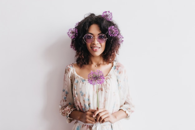 Foto gratuita retrato de interior de atractiva mujer negra con pelo rizado con allium. hermosa chica africana posando con flores de color púrpura.