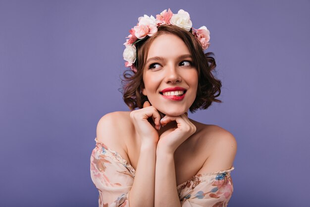 Retrato de interior de una chica romántica con rosas en el pelo corto. Adorable mujer sonriendo juguetonamente.