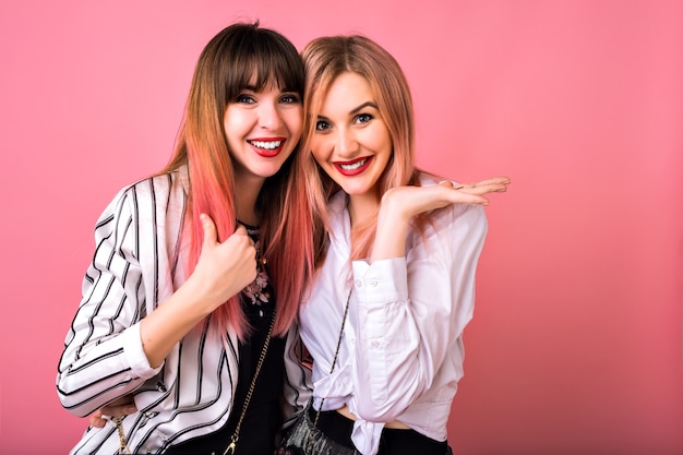 Retrato interior de dos mujeres hermanas felices mejores amigas, vistiendo ropa de moda en blanco y negro y pelos rosados, abrazos y emociones emocionadas, estilo hipster