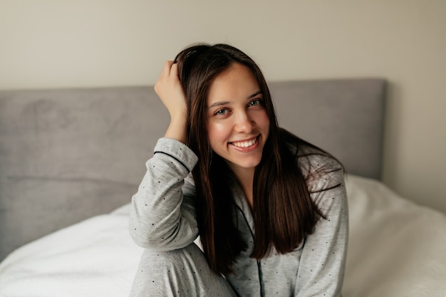 Retrato interior de una encantadora mujer bonita con cabello oscuro sonriendo mientras se despierta por la mañana en casa.