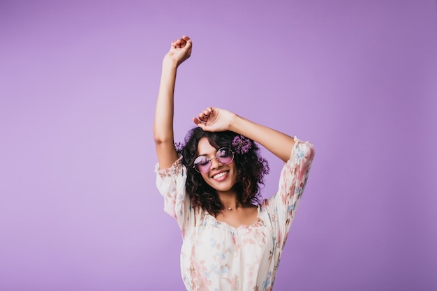 Retrato interior de una magnífica mujer africana de pie con las manos en alto. modelo de mujer con cabello ondulado que expresa buenas emociones.