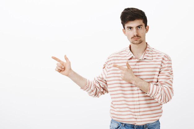 Retrato interior de un novio celoso serio con barba y bigote, apuntando hacia la izquierda con gestos de pistola y mirando, enojado e intenso, de pie