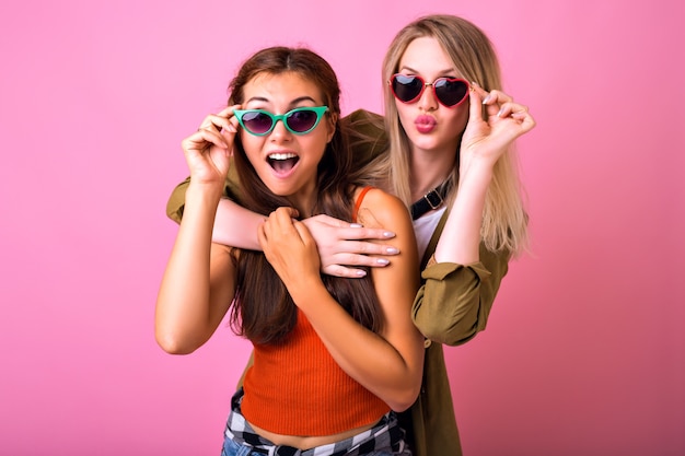 Retrato interior positivo alegre de dos divertidos abrazos de mujer rubia y morena y mirando el uno al otro