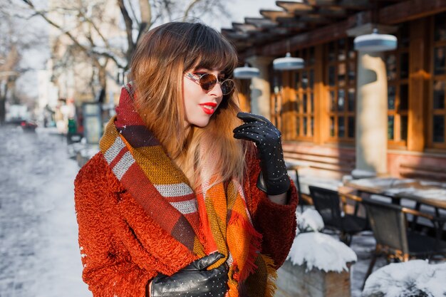 Retrato de invierno de elegante mujer morena con gafas retro posando al aire libre