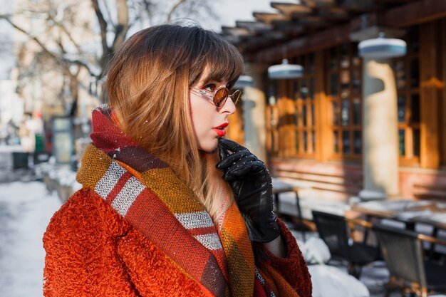 Retrato de invierno de elegante mujer morena con gafas retro posando al aire libre