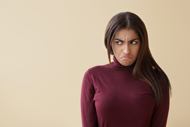 Retrato de irritada joven bella dama afroamericana frunciendo el ceño y mirando a otro lado con expresión de mal humor, sintiéndose disgustado con algo. Ira, molestia, irritación y emociones negativas