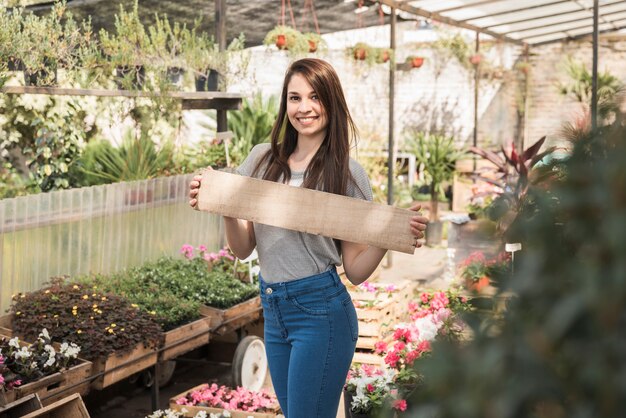 Retrato de un jardinero de sexo femenino feliz con el tablón de madera que se coloca en invernadero