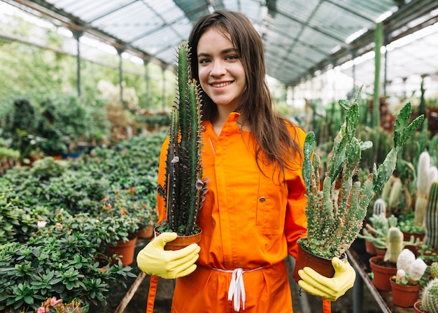 Retrato de un jardinero de sexo femenino joven sonriente que sostiene las plantas en conserva del cactus