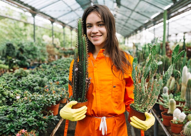 Retrato de un jardinero de sexo femenino joven sonriente que sostiene las plantas en conserva del cactus