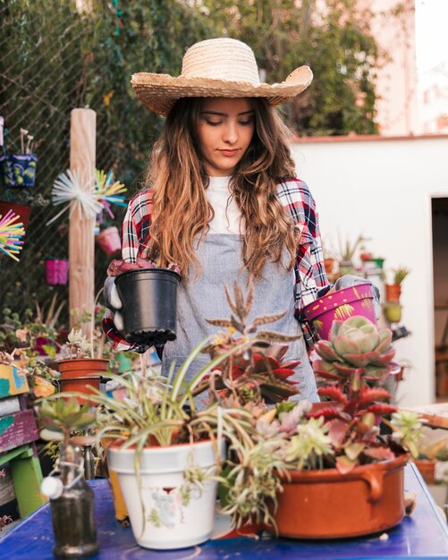 Retrato de un jardinero de sexo femenino que lleva el sombrero que mira las plantas en conserva en la tabla