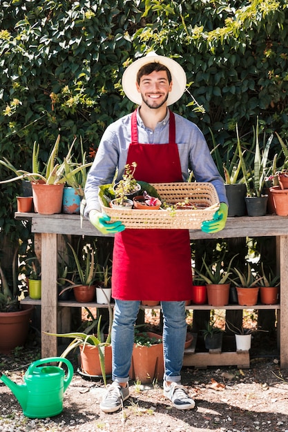 Retrato de un jardinero de sexo masculino joven feliz que sostiene las plantas en conserva en la cesta