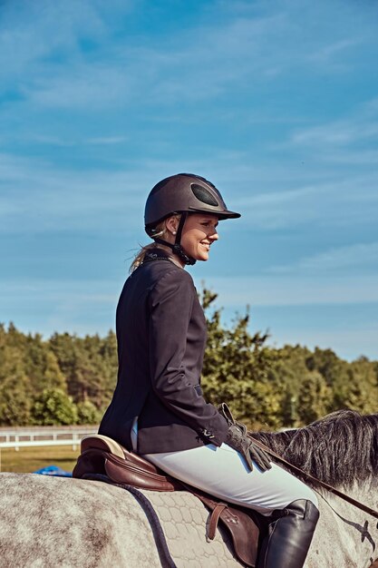 Retrato de una jockey femenina sonriente en un caballo gris moteado en la arena abierta.