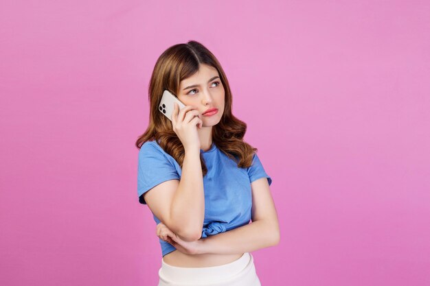 Retrato de una joven aburrida con una camiseta casual hablando por teléfono móvil aislada sobre fondo rosa