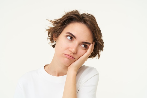 Foto gratuita el retrato de una joven aburrida se inclina con la cabeza en la mano y frunce el ceño, parece molesto y gruñón pensando de pie