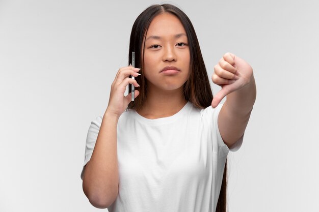 Retrato de joven adolescente hablando por teléfono y mostrando los pulgares hacia abajo