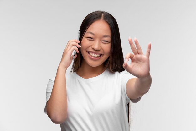 Retrato de joven adolescente hablando por teléfono y mostrando signo bien