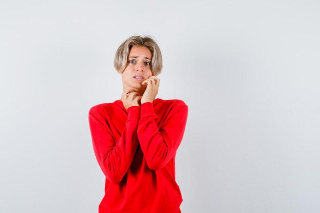 Retrato de joven adolescente con la mano en la mejilla en suéter rojo y mirando asustado vista frontal