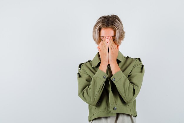 Retrato de joven adolescente con las manos en la cara en chaqueta verde y mirando deprimido vista frontal