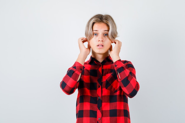 Foto gratuita retrato de joven adolescente con las manos cerca de las orejas en camisa a cuadros y mirando perplejo vista frontal