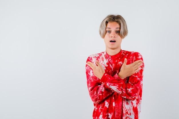 Retrato de joven adolescente manteniendo los brazos cruzados sobre el pecho en camisa y mirando sorprendido vista frontal