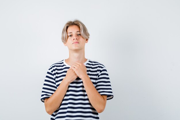 Retrato de joven adolescente manteniendo las manos en el pecho en camiseta a rayas y mirando triste vista frontal